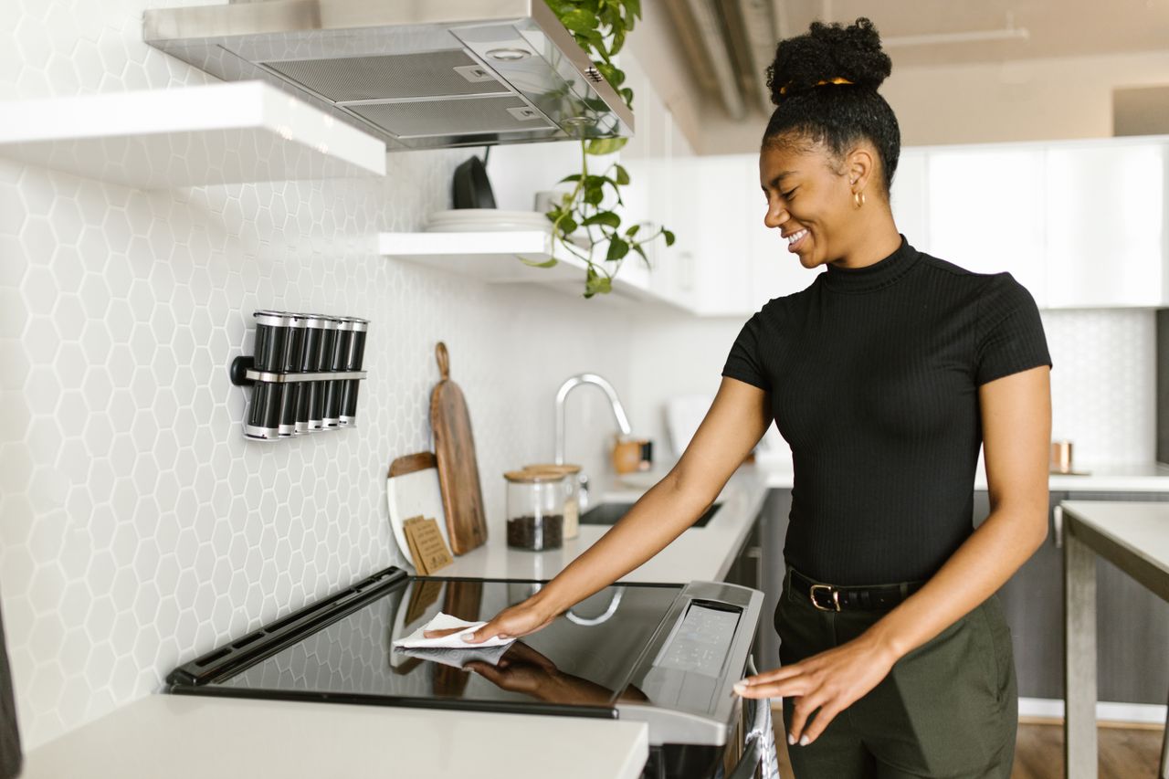 team-04 A woman is cleaning the kitchen stove top, showcasing modern housekeeping and responsibility.